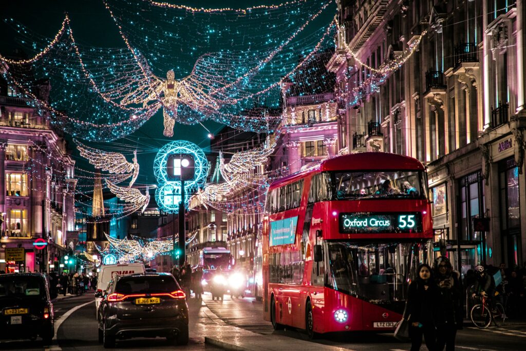 Oxford Street in London during Christmas, featuring angel-shaped lights and decorations, with buses, cars, and people walking along the street